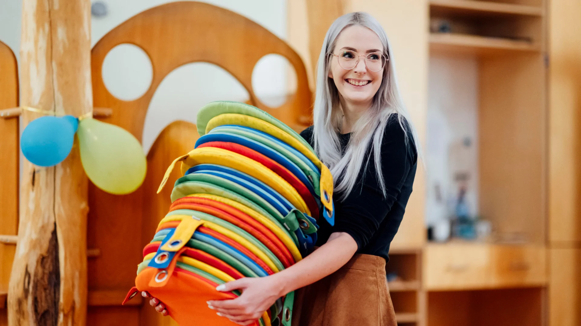 Erzieherin trägt Stapel bunter Sitzkissen im Kita-Raum des Studierendenwerks Oldenburg – Kita Job