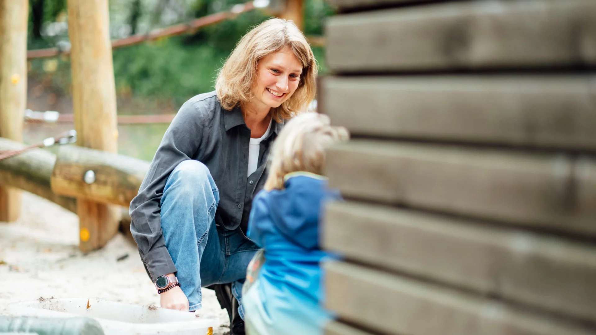 Erzieherin kniet im Außenspielbereich und spricht mit Kind der Kita des Studierendenwerks Oldenburg – Kita Job