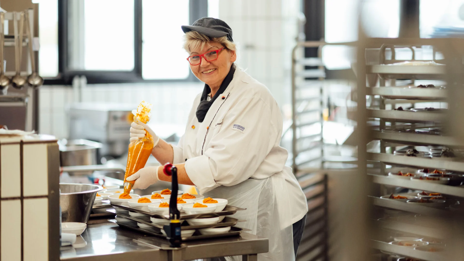Köchin dressiert Möhrenpüree auf Tellern in der Mensaküche des Studierendenwerks Oldenburg – Koch Job