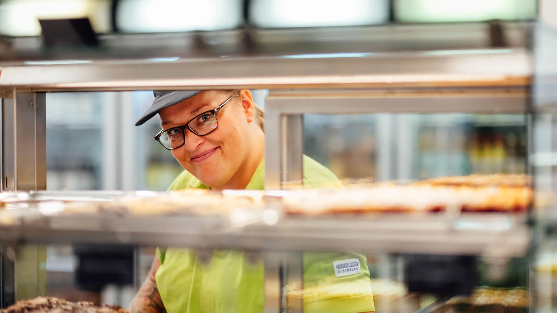 Servicekraft lächelt hinter Snacktheke in der Mensa des Studierendenwerks Oldenburg – Küche & Gastro Job