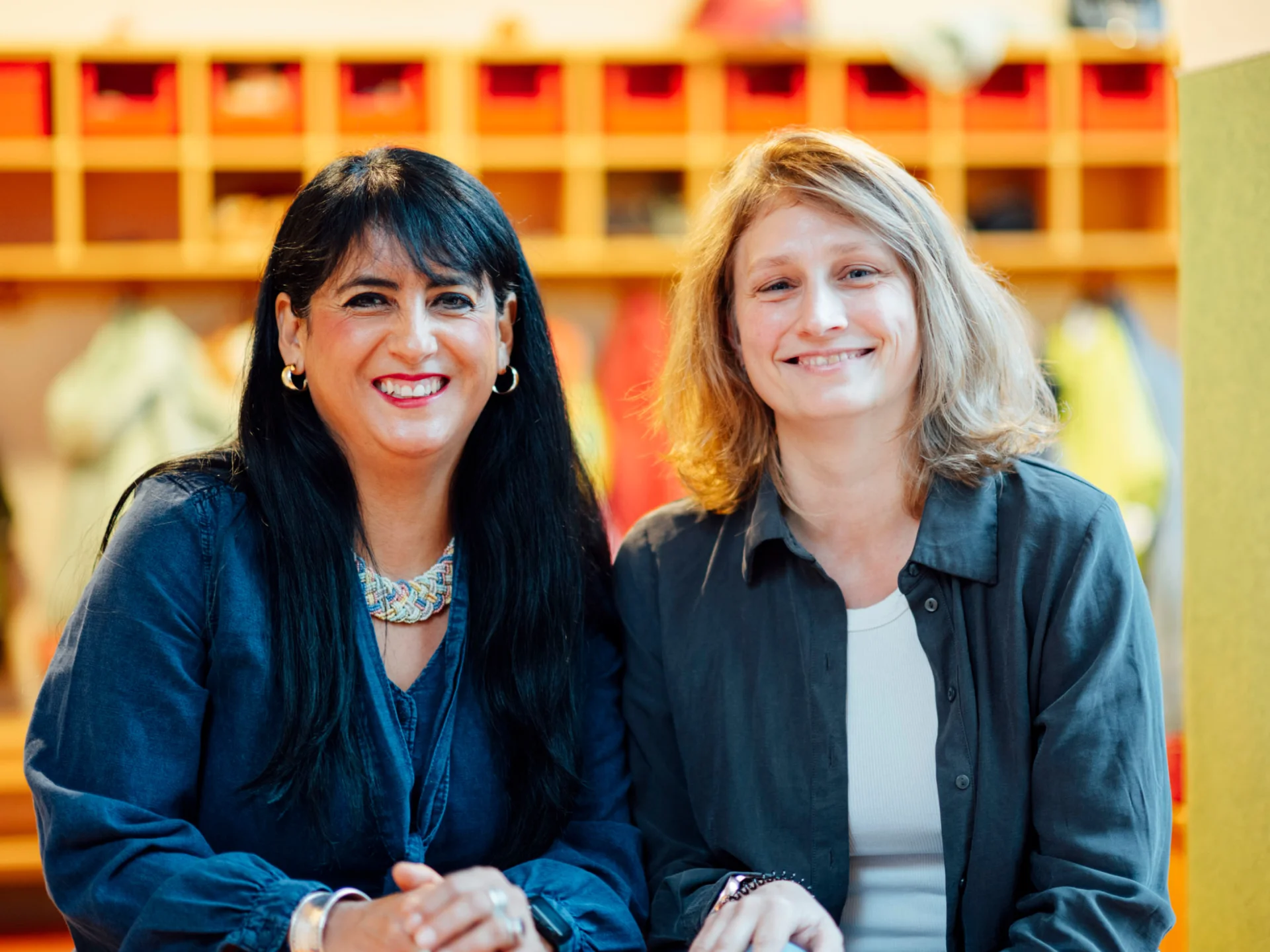 Zwei Mitarbeiterinnen lächeln vor bunten Garderobenfächern des Studierendenwerks Oldenburg – Vorteile Studierendenwerk