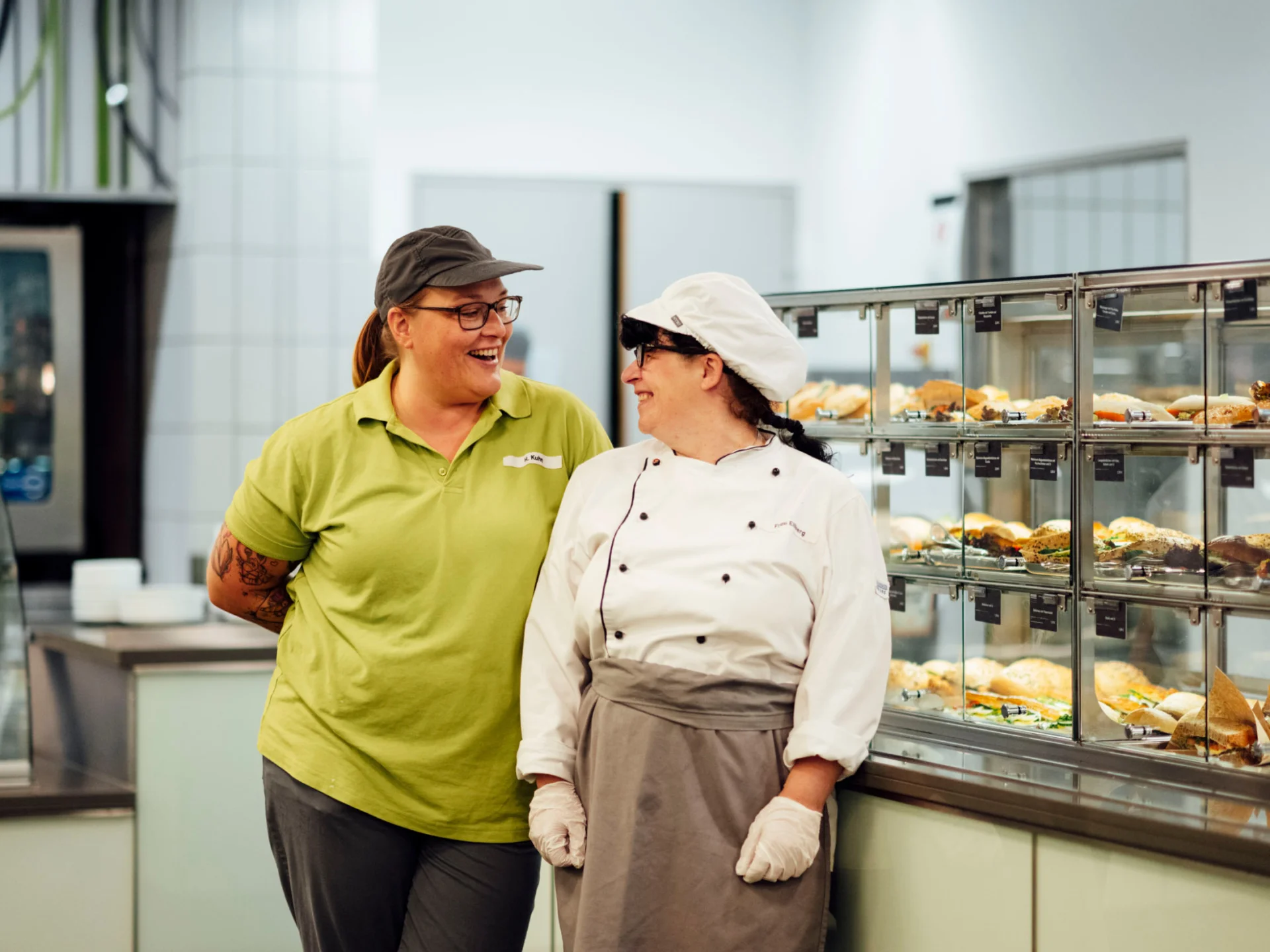 Köchin und Servicekraft lachen vor Snackauslage der Mensa des Studierendenwerks Oldenburg – Vorteile Studierendenwerk